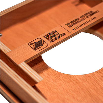 Close-up of wooden cornhole board featuring American Cornhole Association logo and unique hole design.